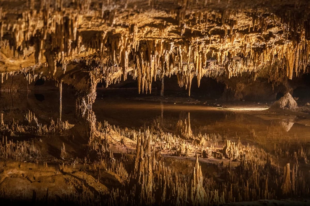 Underground cave with golden stalactites reflected in a still pool.